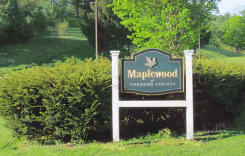 Maplewood Nursing Home entrance sign beside green hedges and trees.