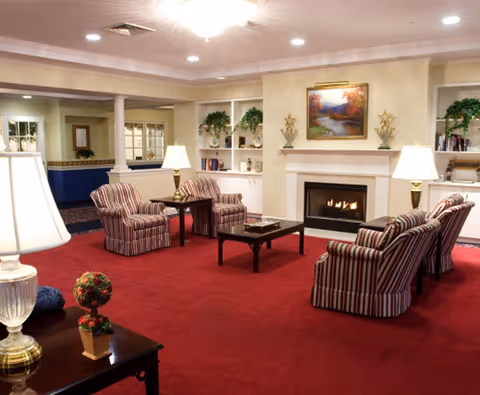 A cozy lounge with striped armchairs and tables arranged around a coffee table facing a fireplace and built-in bookshelves.