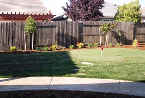 Well-kept backyard lawn with a wooden fence and small trees along the edge.