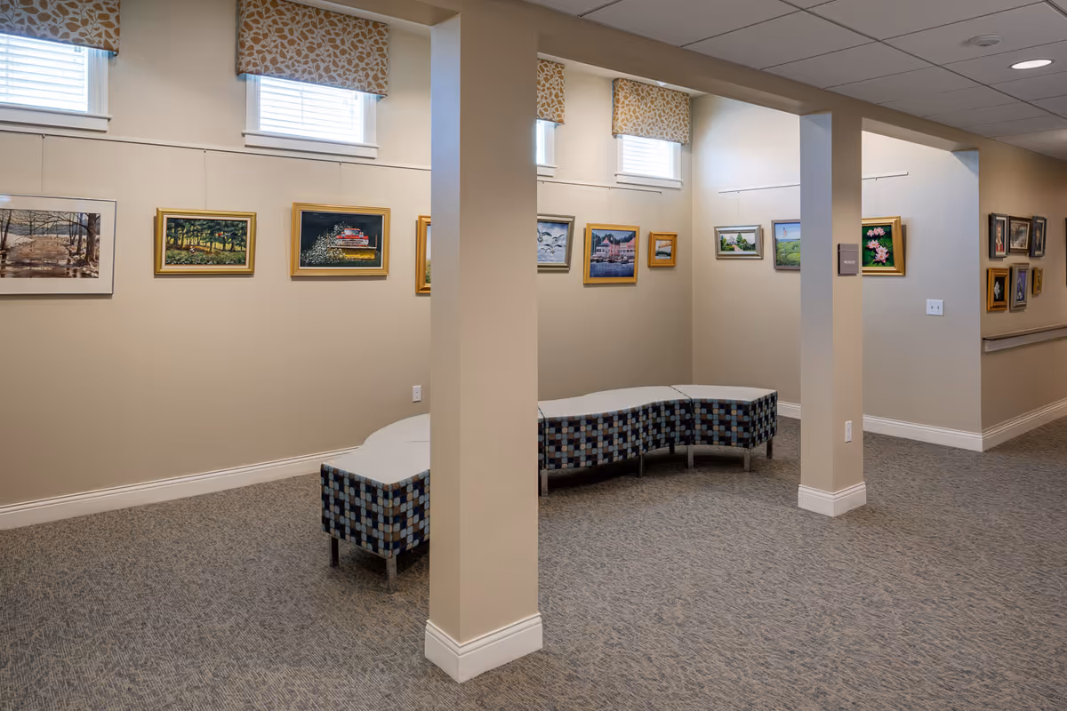 Well-lit interior gallery area with framed paintings on the walls and curved upholstered benches.