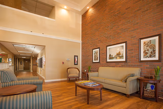 Seating area with a sofa, armchairs and coffee table against a brick accent wall in a facility lounge.