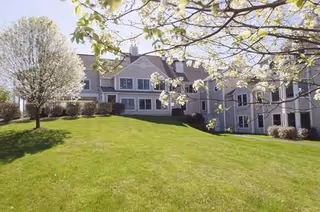 Gray multi-story building with white trim set behind a green lawn and blooming trees.