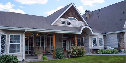 Exterior view of a residential-style building with a covered porch, multiple windows, and a well-maintained lawn under a partly cloudy sky.