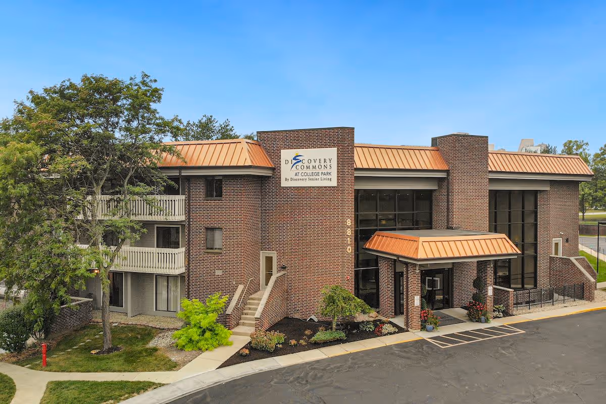 Front exterior of a two-story brick senior living building with a covered entrance, balconies, and landscaping.