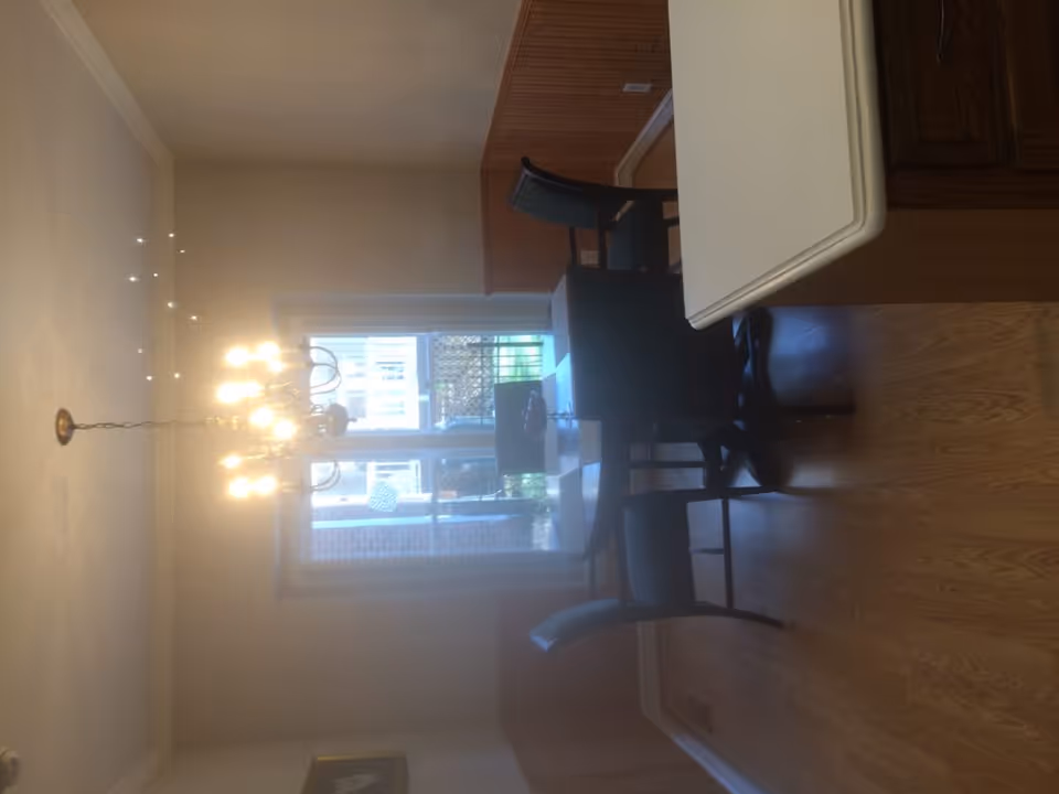 Dining room with a chandelier over a table and chairs by a window and hardwood floors.