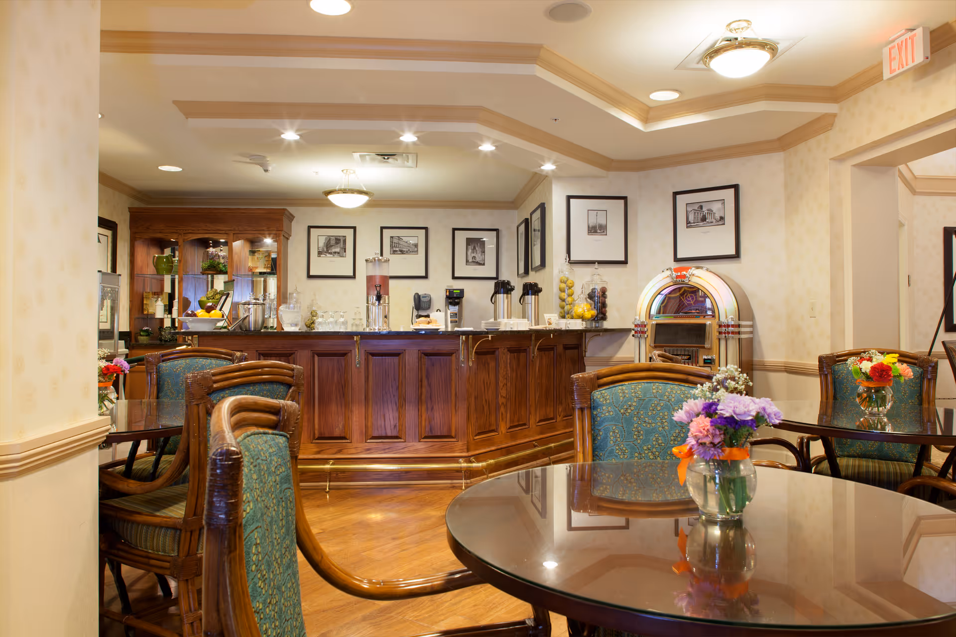 Cozy dining/lounge area with round tables and floral centerpieces facing a wooden service bar and jukebox.