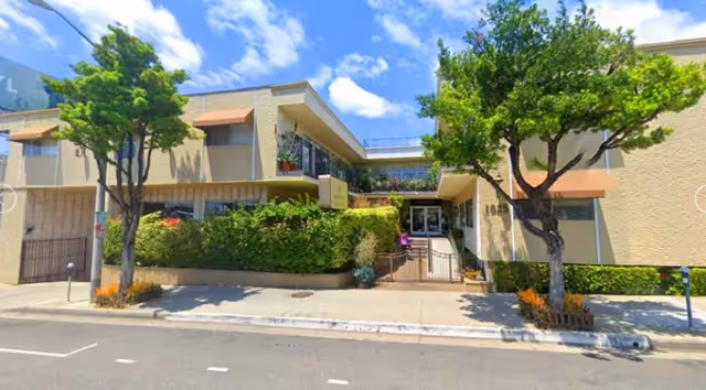 Exterior view of Savant of West Hollywood with trees, shrubs, and building entrance.