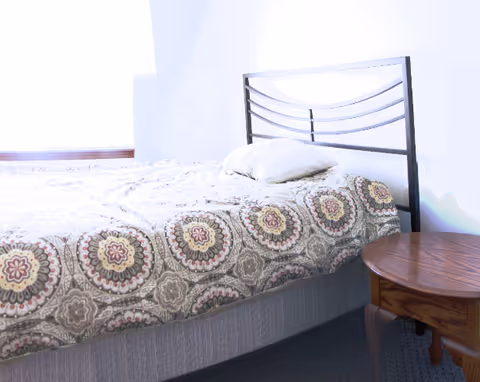 A bedroom with a patterned bedspread on a bed with a metal headboard, a pillow, and a wooden bedside table.