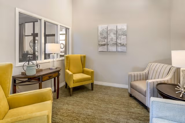 Small sitting room with yellow armchairs, a striped armchair, side tables, lamps, and wall art.