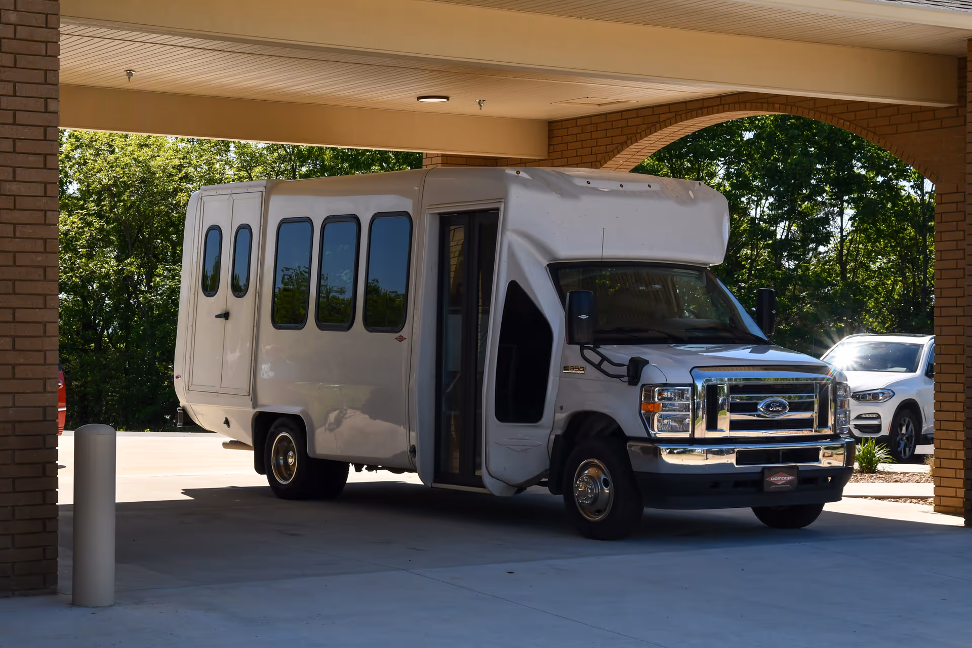 White passenger shuttle van parked under the covered entrance/porte-cochere of a healthcare facility.