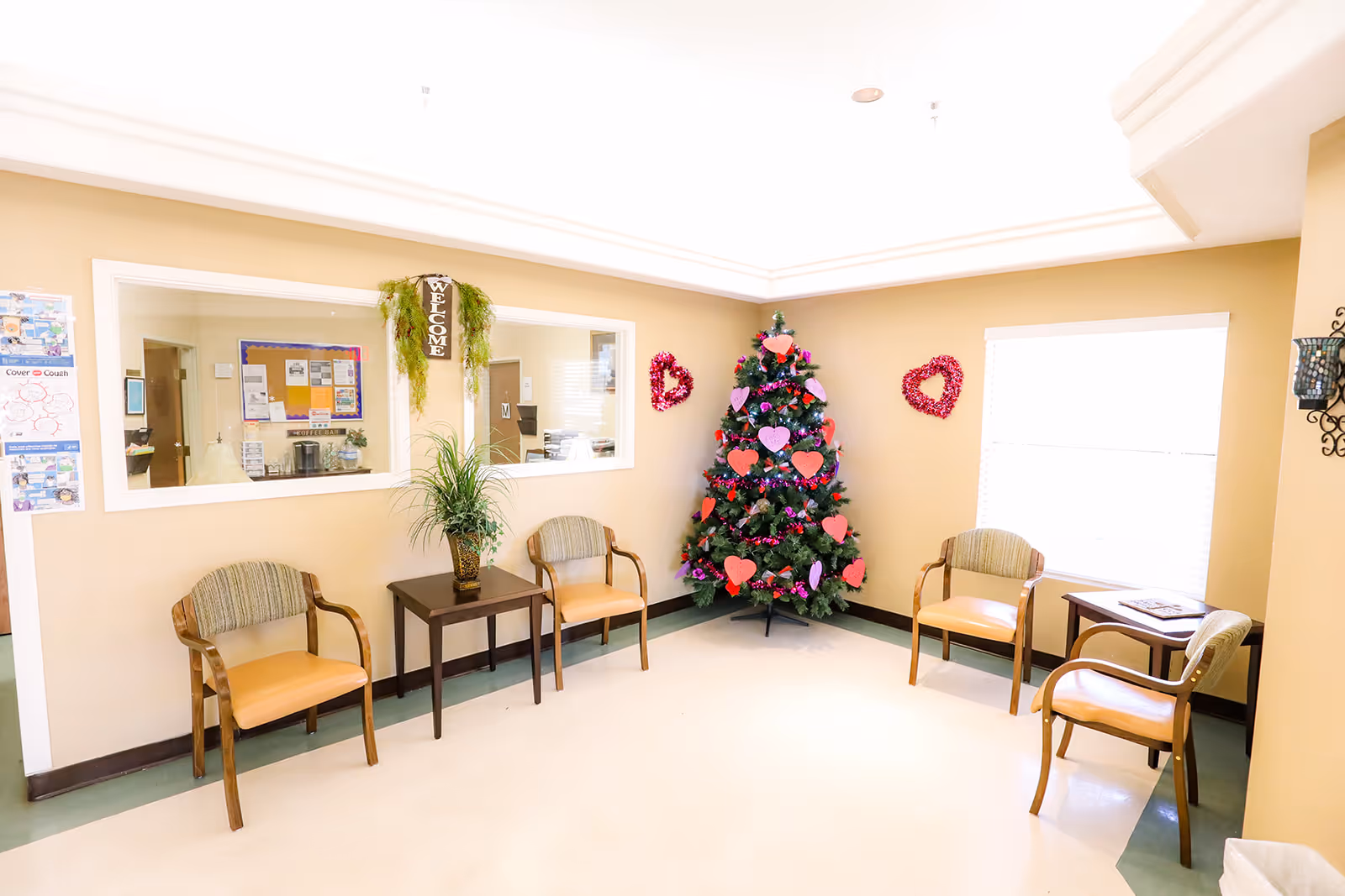 A bright reception/waiting area with several chairs, a small table and a decorated Christmas tree against a beige wall.