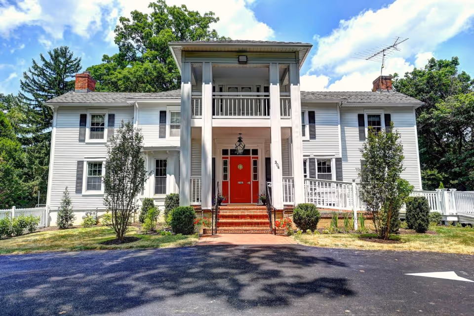Front view of a white two-story colonial-style building with columns, a red front door, and a driveway.