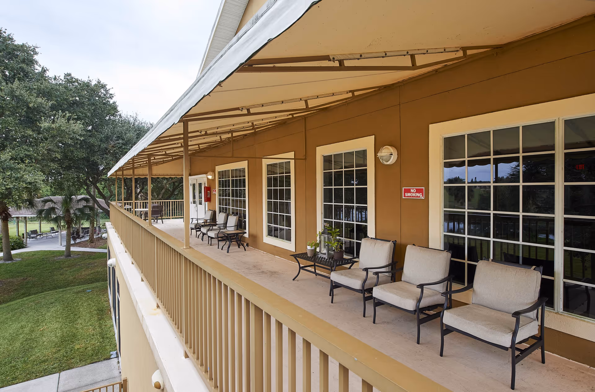 Covered second-floor exterior walkway with cushioned chairs and small tables overlooking landscaped grounds.