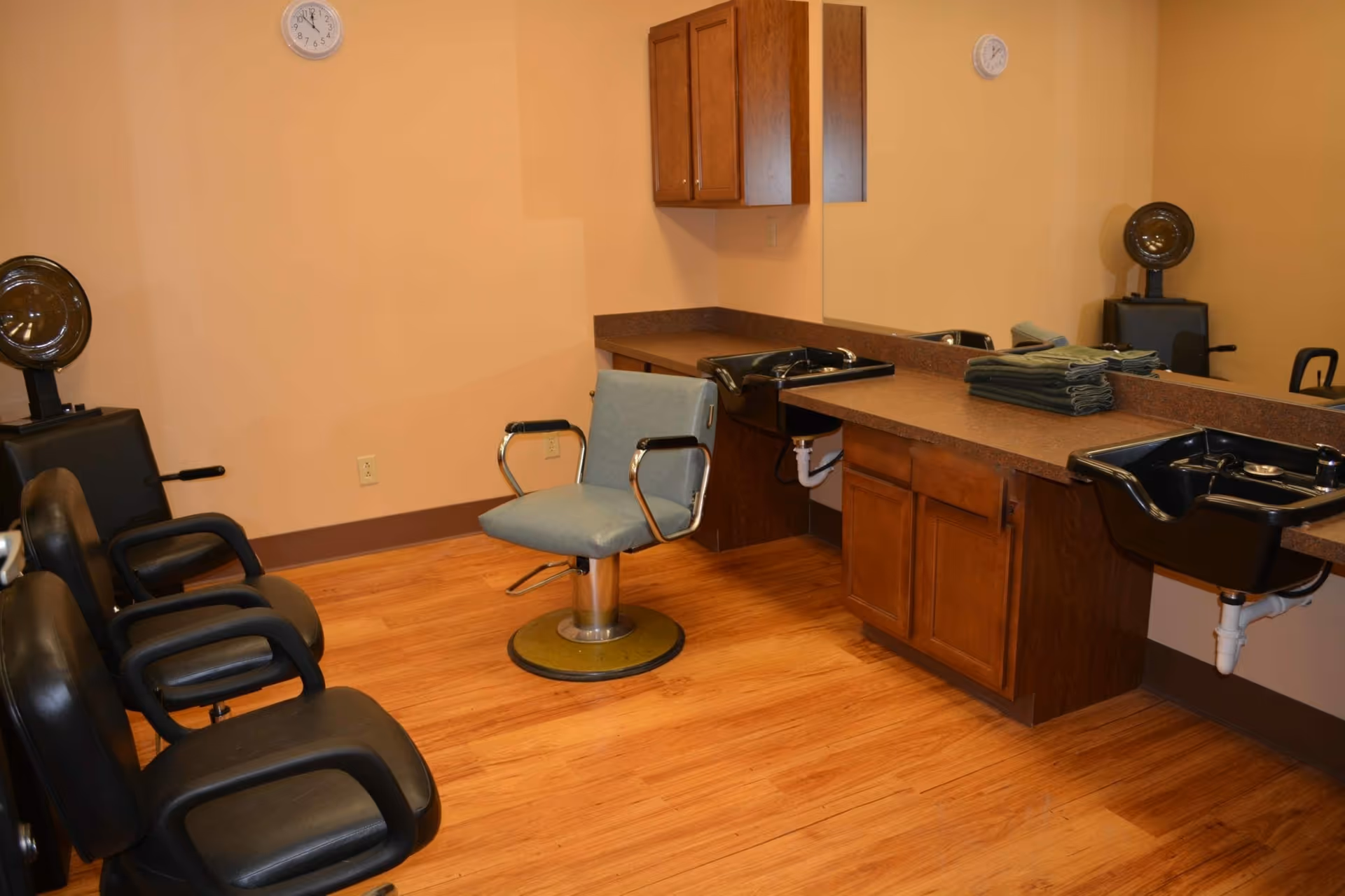 Interior salon/hair-styling room with chairs, shampoo sinks, mirrors and cabinets on wood flooring.