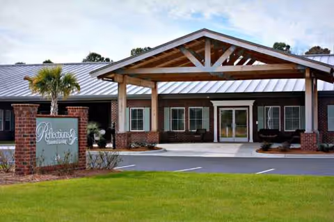 Exterior view of Reflections Assisted Living at Carolina Forest entrance with brick pillars and wooden portico.