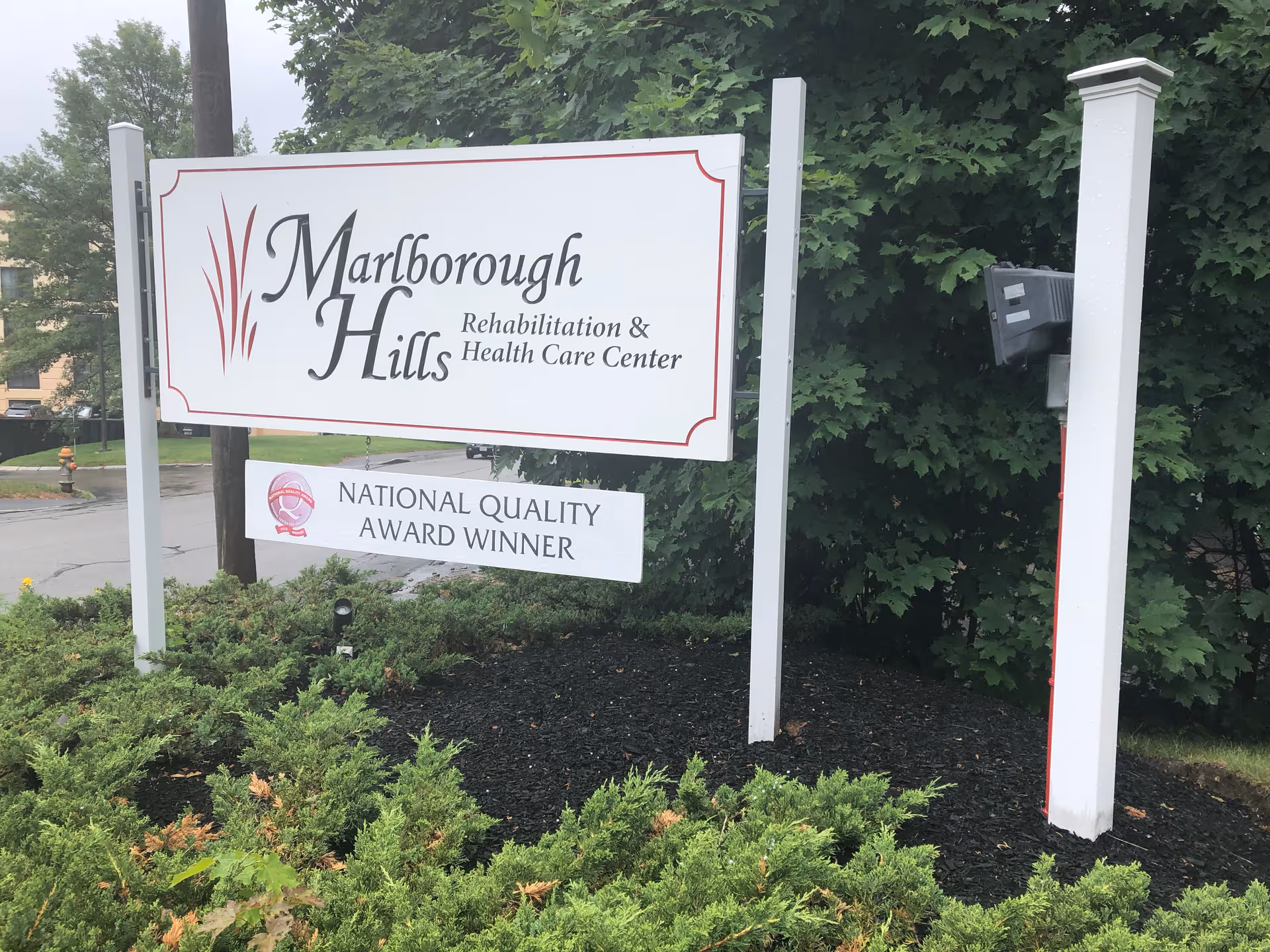 Entrance sign for Marlborough Hills Rehabilitation & Health Care Center with a "National Quality Award Winner" placard surrounded by landscaping.