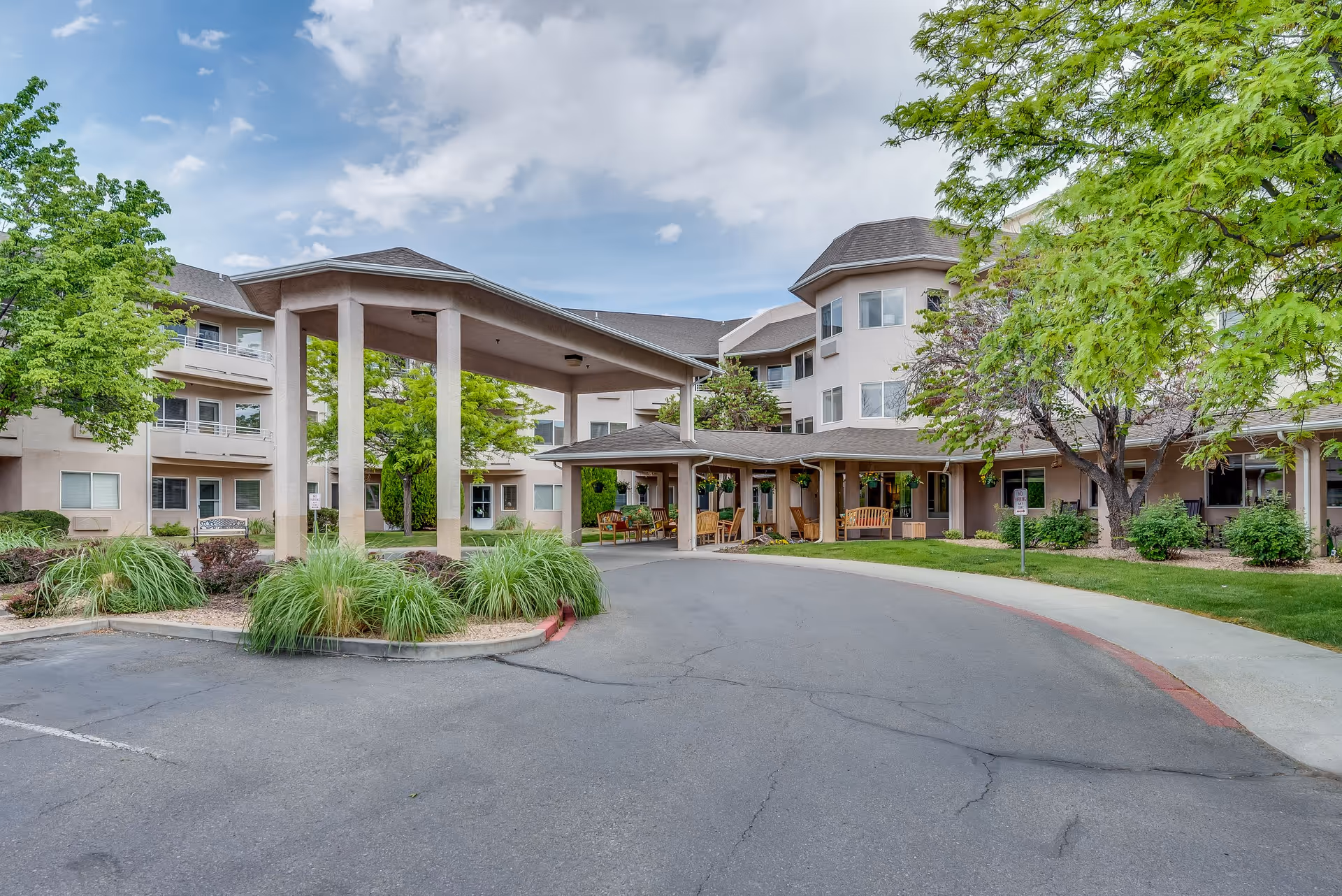 Exterior view of Solstice Senior Living at Grand Valley showing the entrance with a covered drop-off area, surrounded by trees and greenery under a partly cloudy sky.