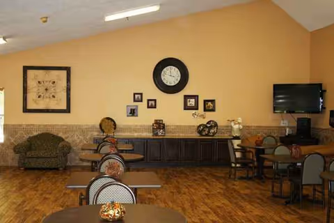 A spacious senior living common area with tables, chairs, a couch, and wall decor.