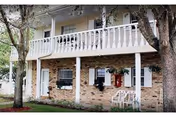 Brick two-story building with white railing balcony and trees in front.
