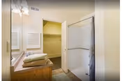 Small bathroom with a vanity and mirror, a shower stall, and an open door leading to a walk-in closet.