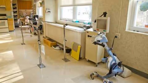 Rehabilitation therapy room with parallel bars, a stationary bike, and medical equipment.