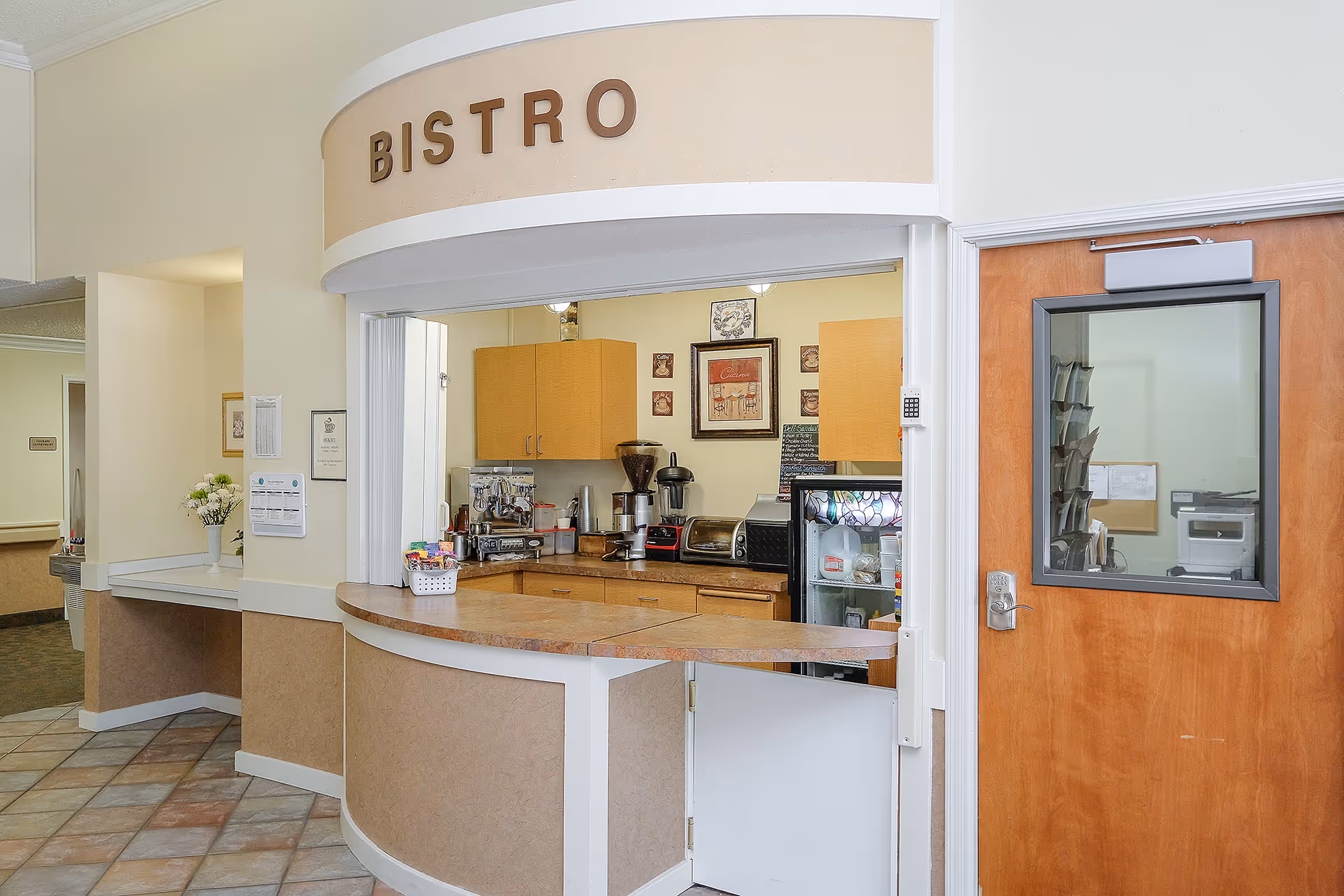 Interior bistro counter area with a curved service window, coffee equipment and cabinets.