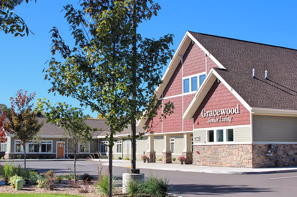 Front exterior of the Gracewood Senior Living building with a pitched roof, sign, trees, and landscaped entrance.
