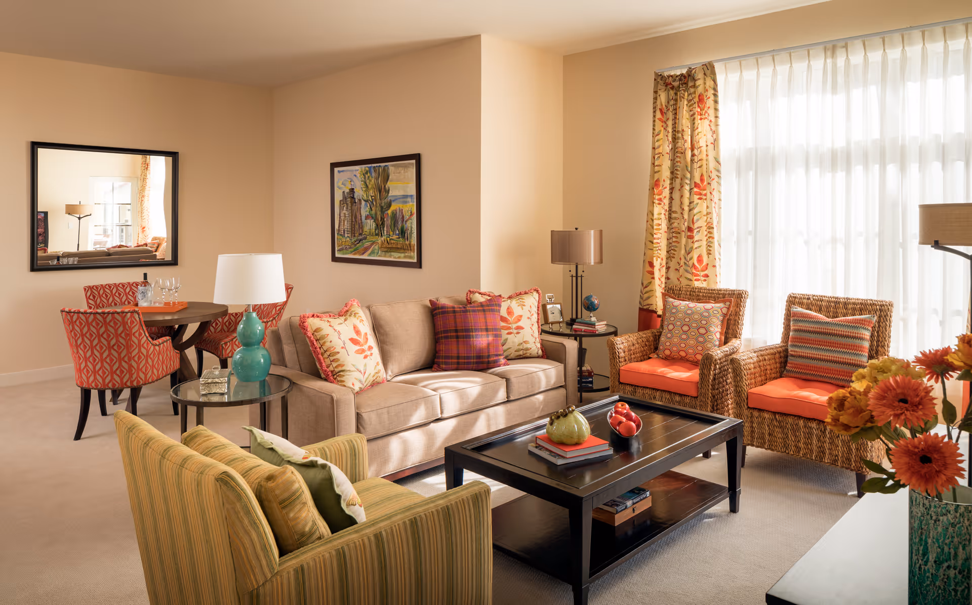 Bright, warmly decorated living room with a sofa, wicker armchairs, coffee table, and a small dining nook.