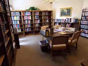 A quiet library room with bookshelves, chairs, and a desk in a residential facility.
