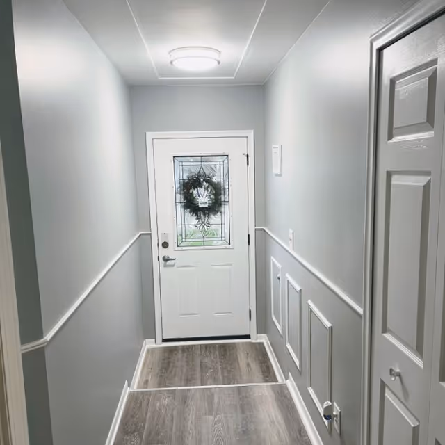 Bright hallway with wainscoted walls leads to a front door adorned with a wreath.