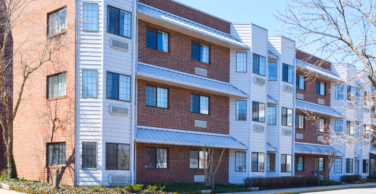 Exterior view of a four-story brick-and-white senior living building with rows of windows and metal awnings.