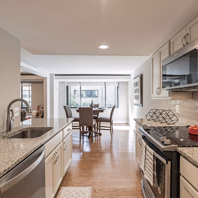 Bright open kitchen with granite countertops, stainless appliances and a dining table by large windows.