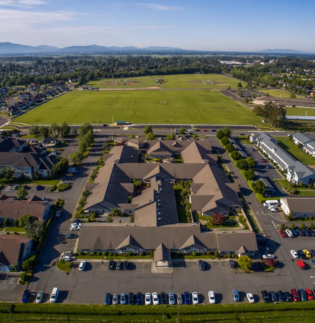 Aerial view of a senior living complex with a parking lot in front and large green fields behind.