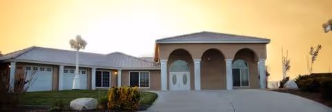 Front view of a single-story assisted living facility with arched entrance and driveway.