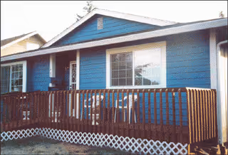 Blue single-story building with a wooden porch railing and windows on the front exterior.