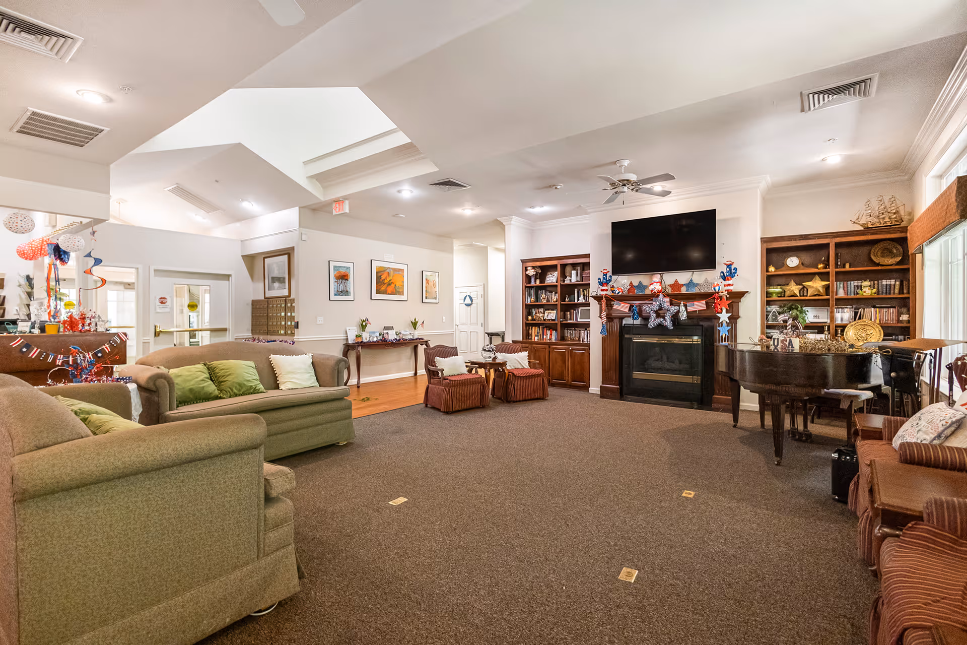 Spacious communal living area with sofas, bookshelves, a fireplace topped by a TV, and a grand piano.