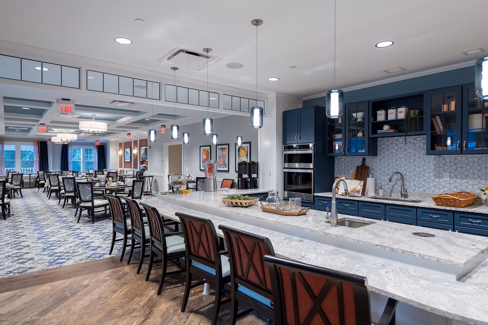 Modern communal dining area with a long marble-topped kitchen island, bar stools, pendant lights, and dining tables in the background.