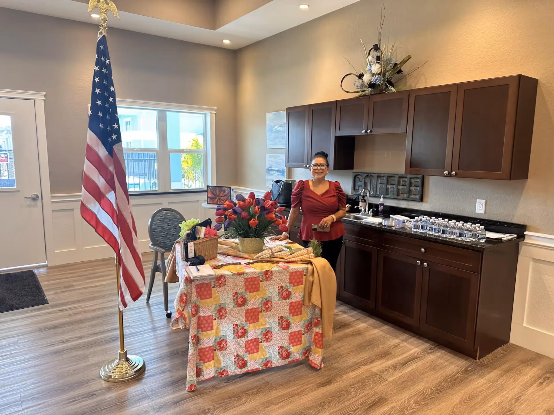 Staff member stands by a decorated table with flowers in a kitchenette area.