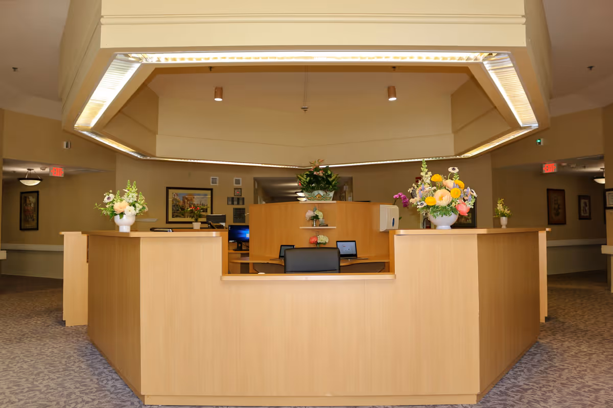 Wooden reception desk in a well-lit interior lobby with floral arrangements and overhead lighting.