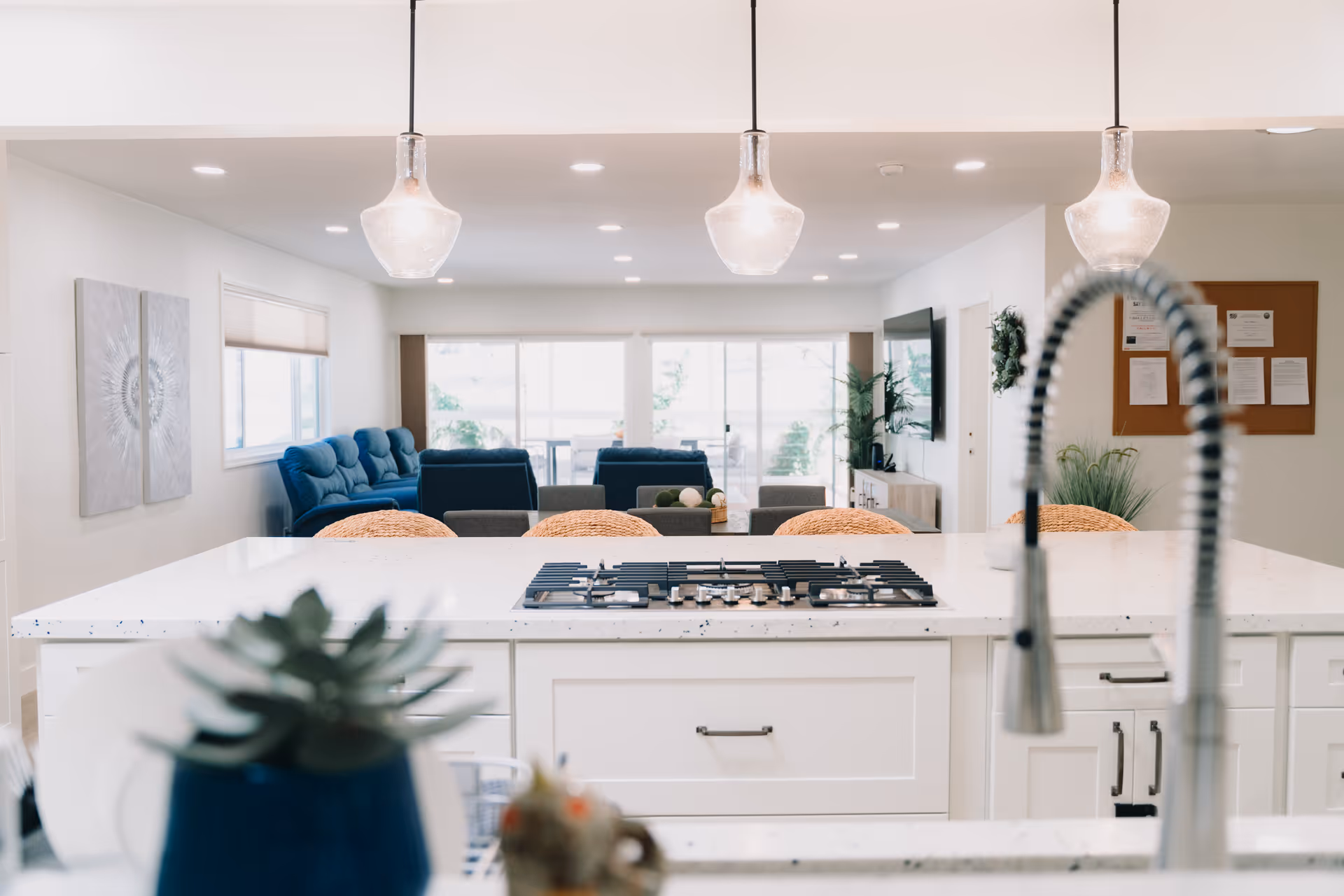 Bright open kitchen with a white island and gas cooktop, pendant lights, and a view into a living area with blue sofas.