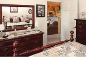 A traditional bedroom with a wooden bed, matching dresser and mirror, and a view into an adjacent living area.