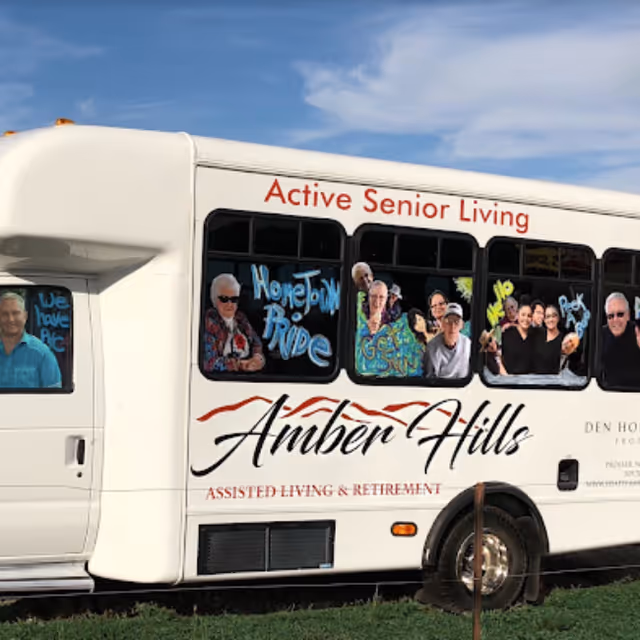 White bus with Active Senior Living Amber Hills branding parked on grass under blue sky.