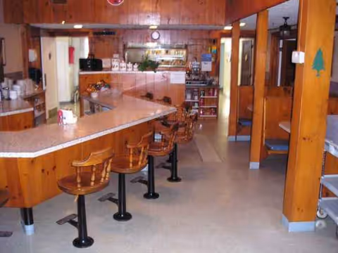 A wooden diner-style dining area with long counter and bar stools inside a senior living facility.