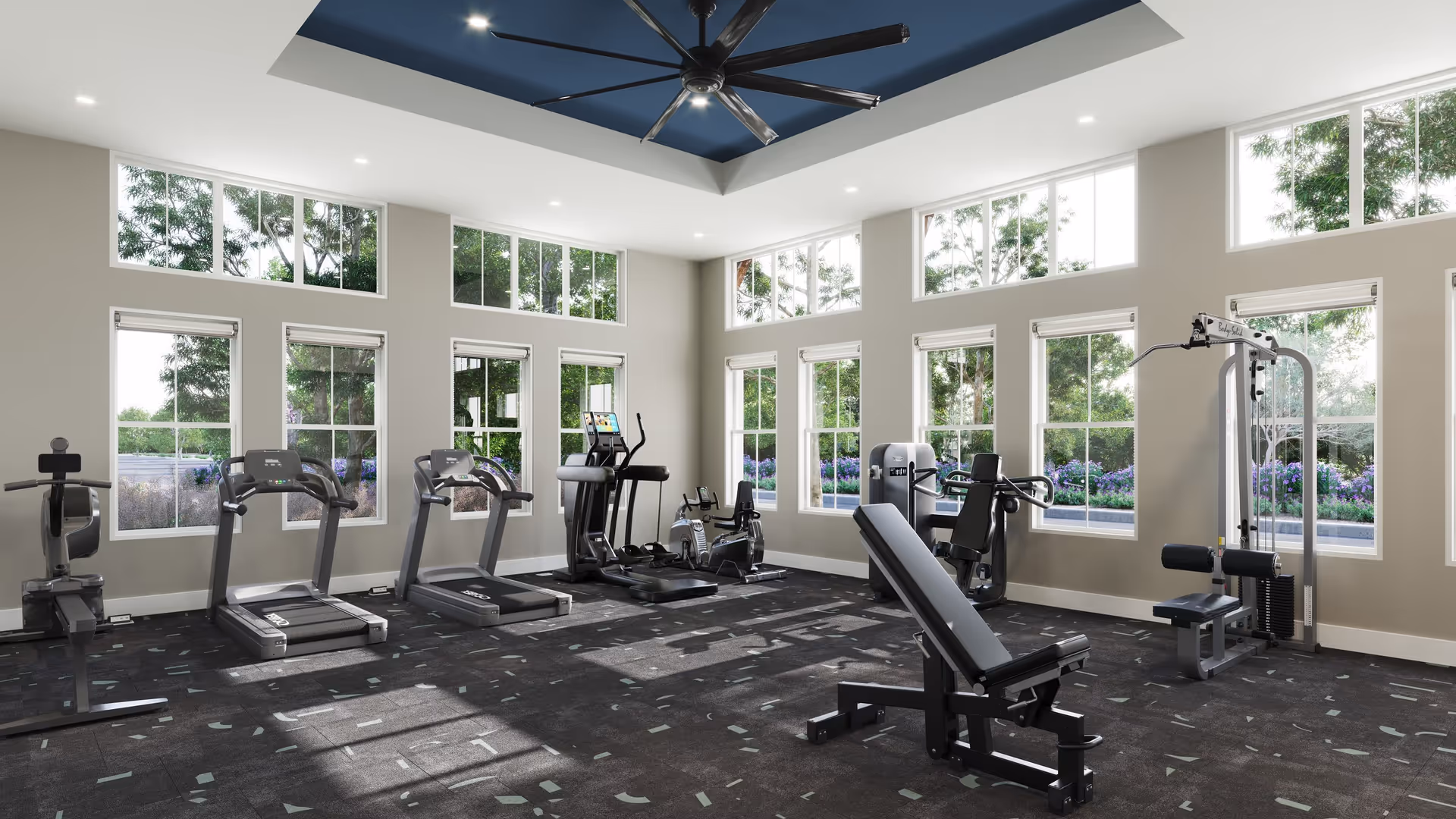 Fitness center with treadmills, a weight bench, resistance machines and large windows letting in natural light.