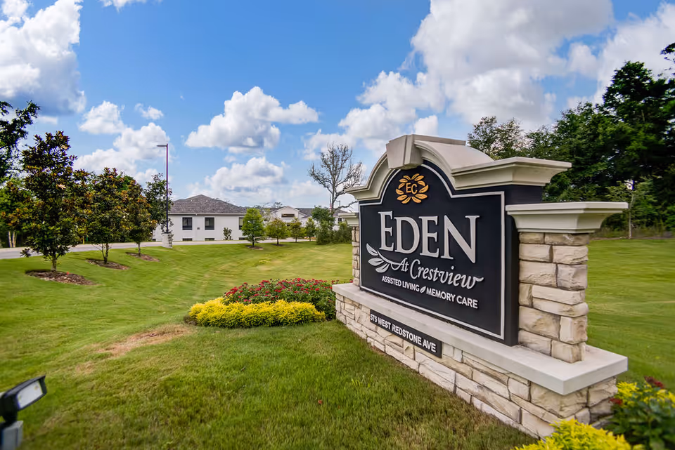 Stone entrance sign for 'Eden at Crestview Assisted Living & Memory Care' on a grassy lawn with the facility building and trees in the background.