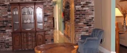 Brick-walled common area with wooden cabinet, round table, and blue armchairs.