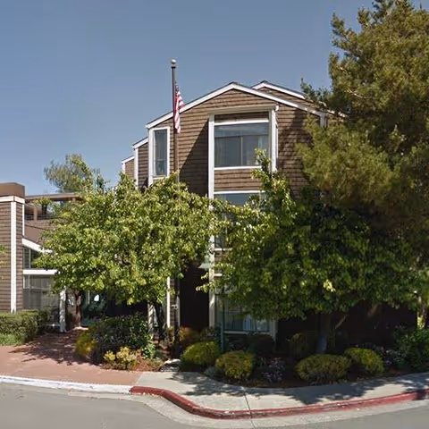 Two-story brown senior living building with landscaping and an American flag.