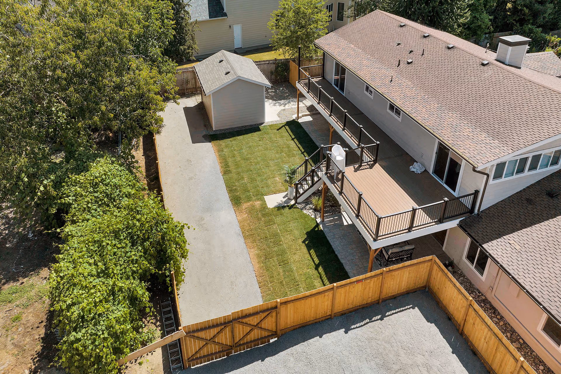 Aerial view of a home's fenced backyard with a deck, lawn, shed, and driveway.