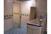 Tiled assisted bathing room with a walk-in tub, shower curtain, grab bars and blue-accented tiles.