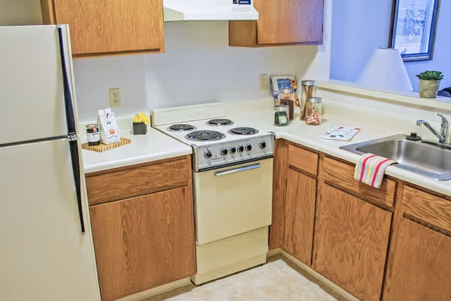Small kitchen with a white electric stove, refrigerator, sink, and wood cabinets with countertops.
